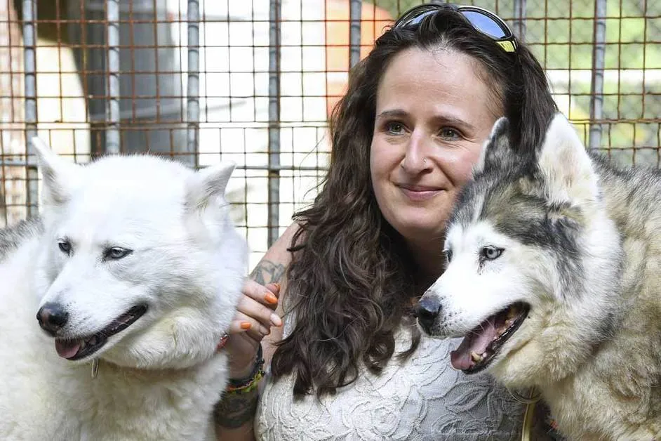 Carine, présidente et fondatrice, entourée de deux chiens devant un enclos du refuge
