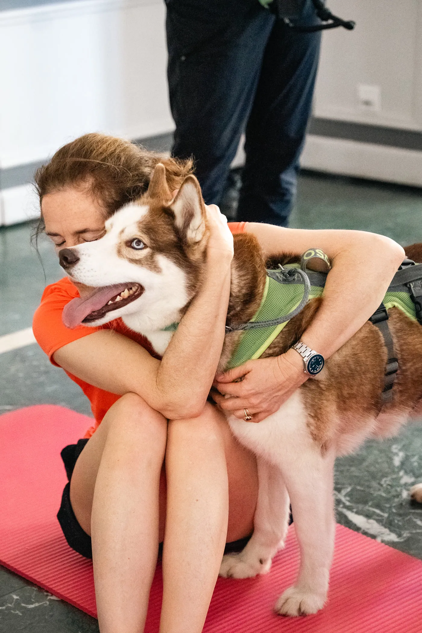 Une participante assise sur un tapis de yoga, les yeux fermés, serrant contre elle un husky brun et blanc qui porte un harnais vert